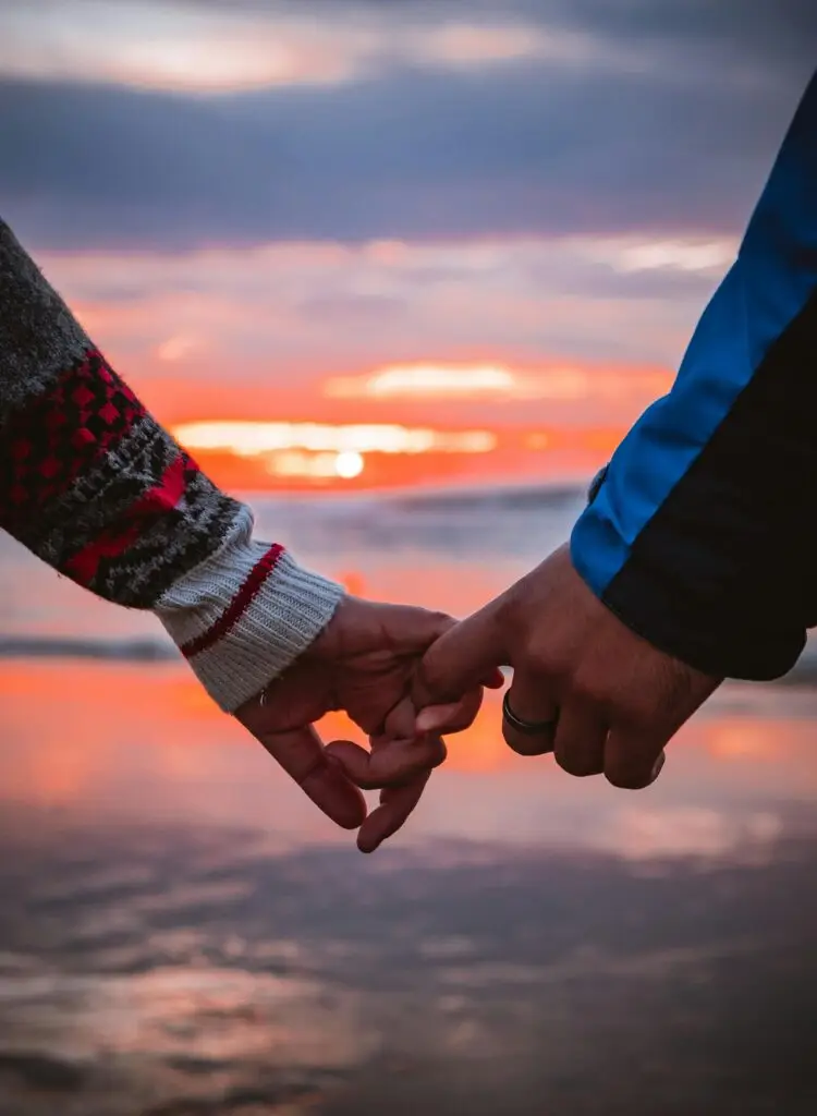 Close-up of a couple holding hands by the beach during a warm sunset.